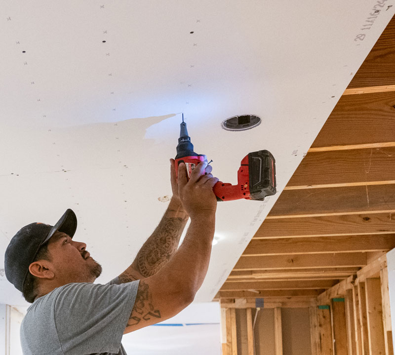 Man-installing-drywall-to-ceiling Man installing a sheet of drywall to the ceiling in a basement